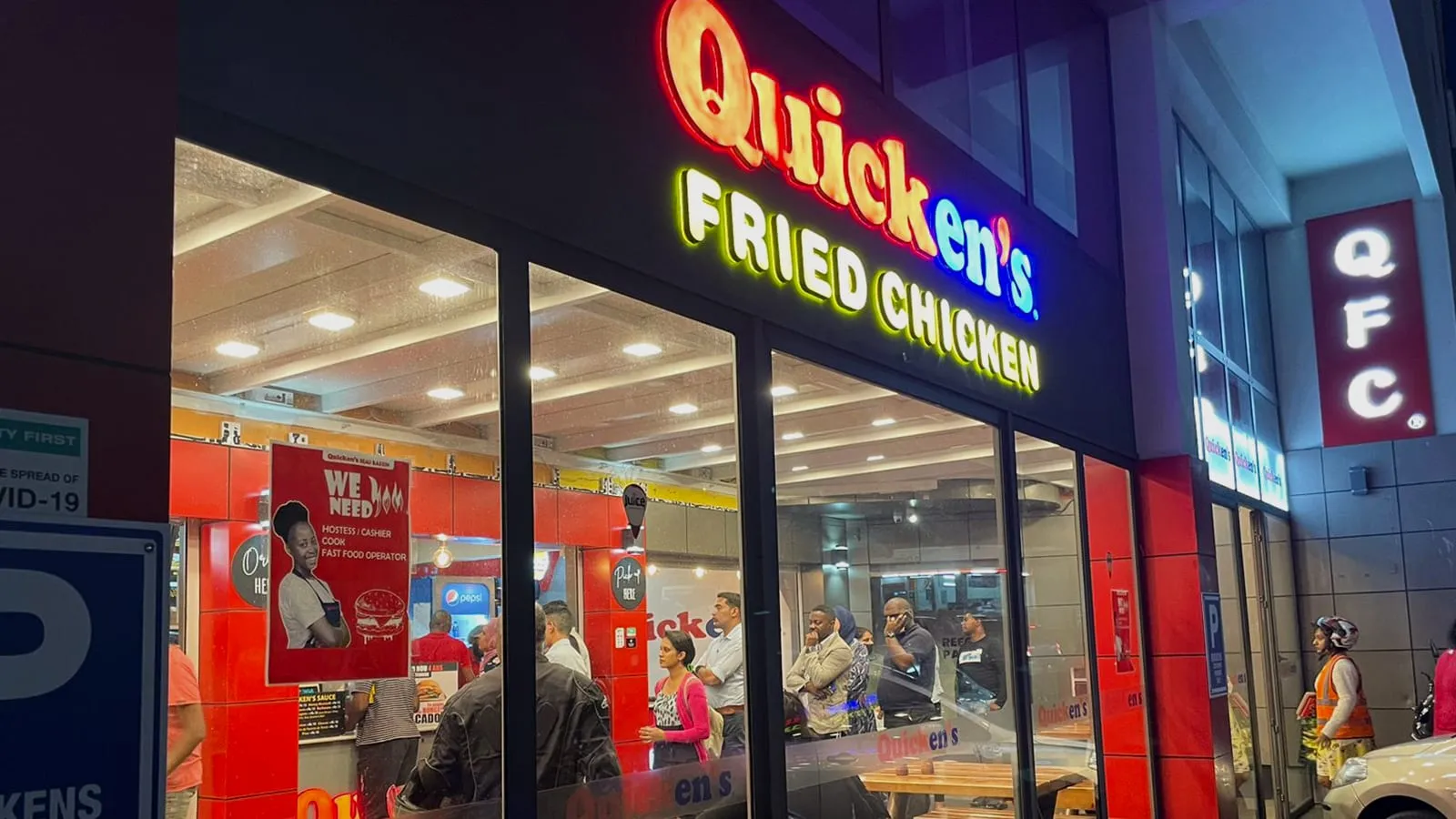The Beau Bassin Quicken’s Fried Chicken at night, its lit sign above a busy glass front