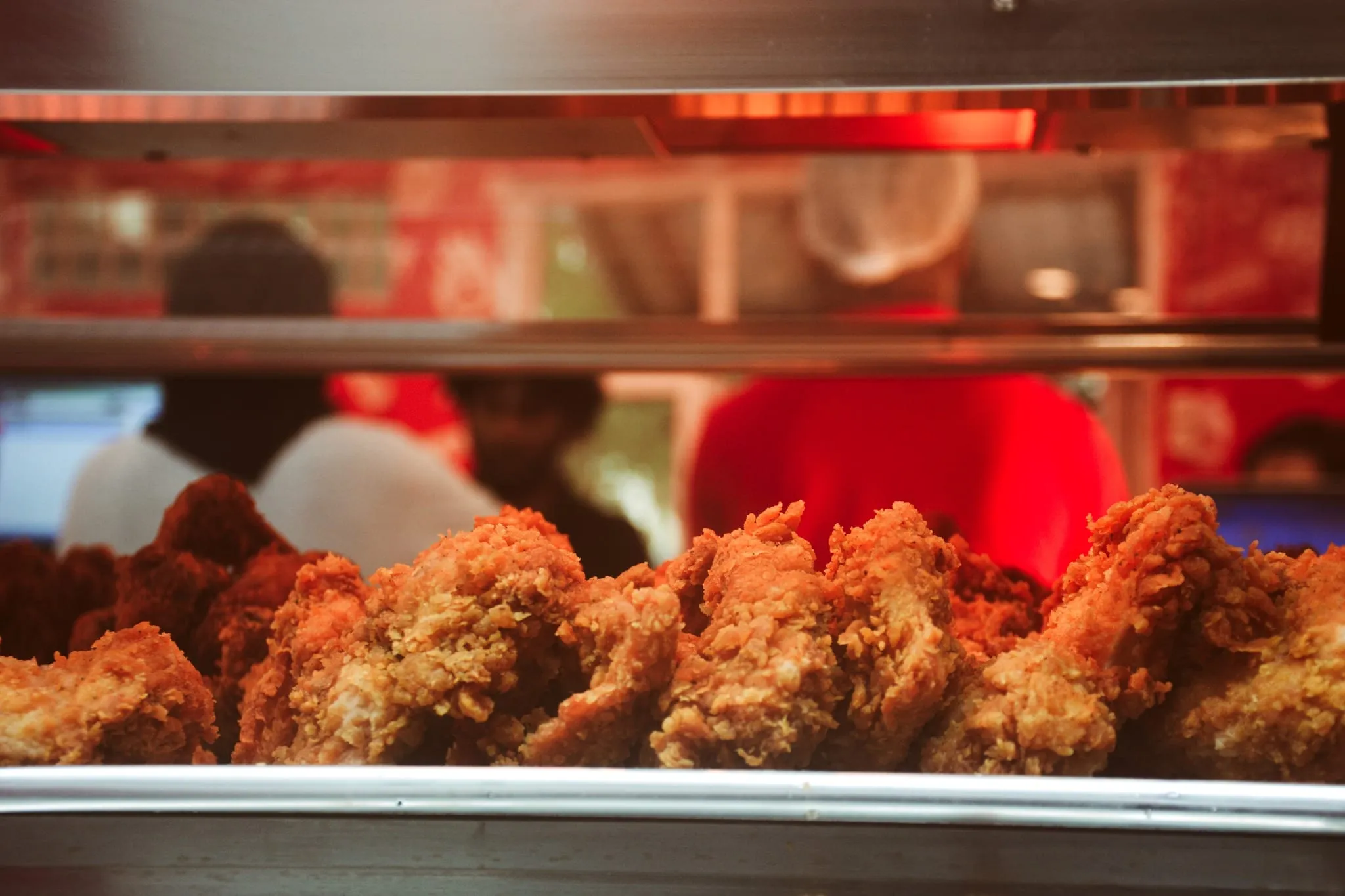 A tray of freshly fried chicken pieces behind the counter, crew working in the background