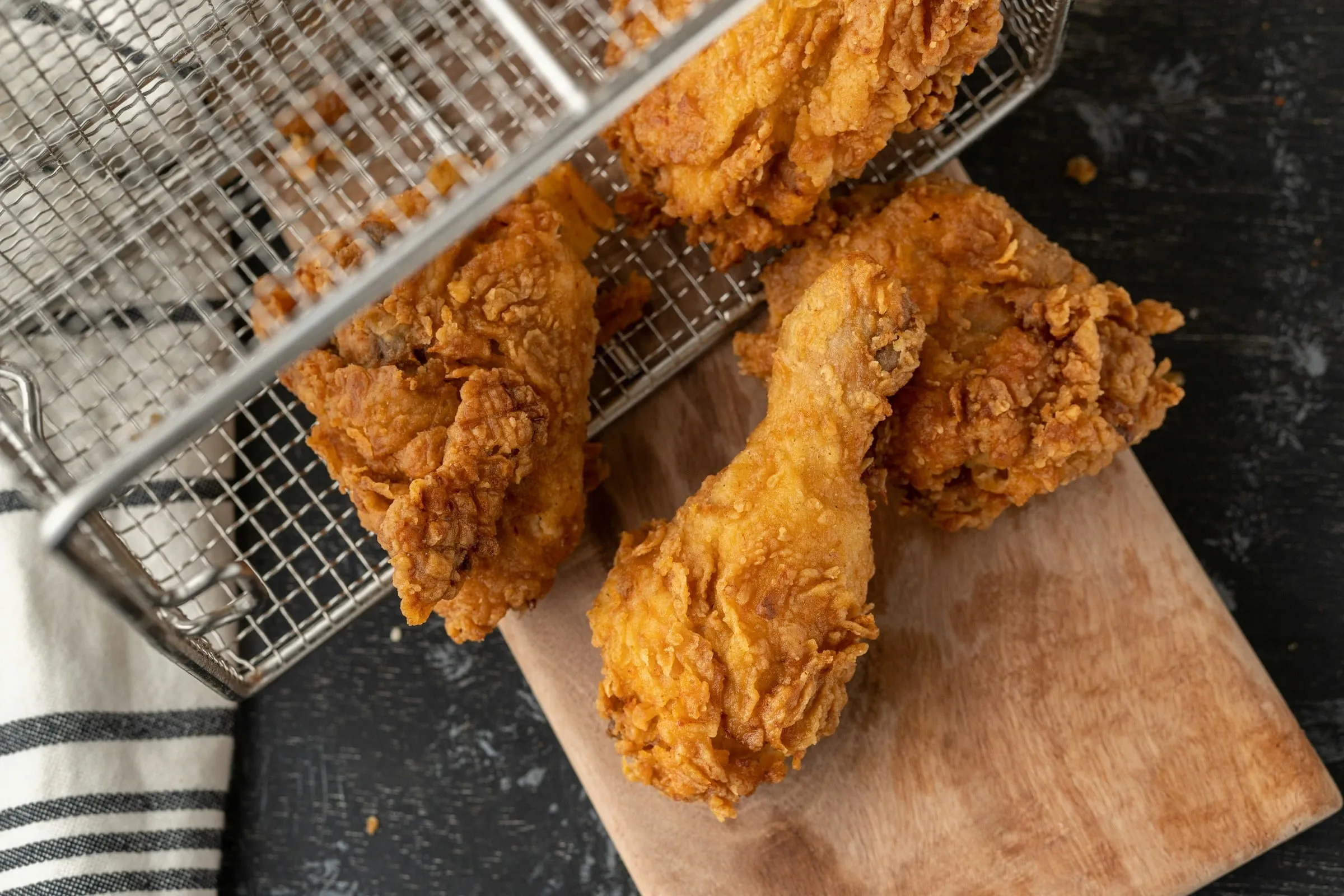 Crispy fried chicken pieces spilling from a fryer basket onto a wooden board
